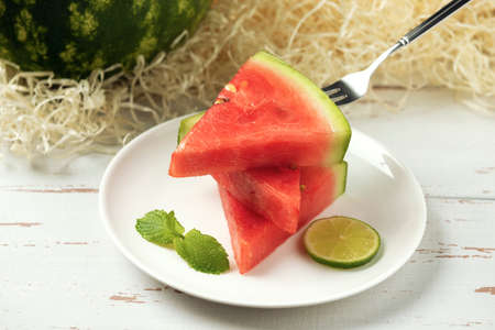 White plate with watermelon slices, mint and lime on the white wooden Provence style background.の写真素材