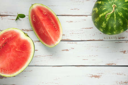 One whole watermelon with pieces of sliced one on the white wooden Provence style background. Flat lay. Top view.の写真素材