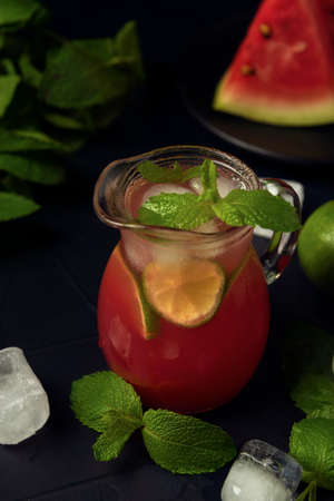 Glass jug with watermelon juice, ice, mint and watermelon slices on the dark textured backdrop.の写真素材