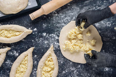 Woman in black gloves spread the cheese filling on the dough. Process of making bakery. The Adjarian Khachapuri Recipe â Georgian cheese bread. Top view. Flat lay.の写真素材