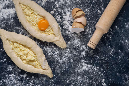 Two raw khachapuri with egg yolk ready for baking on blue textured backdrop. Process of making bakery. The Adjarian Khachapuri Recipe â Georgian cheese bread. Top view. Flat lay. Space for text.の写真素材