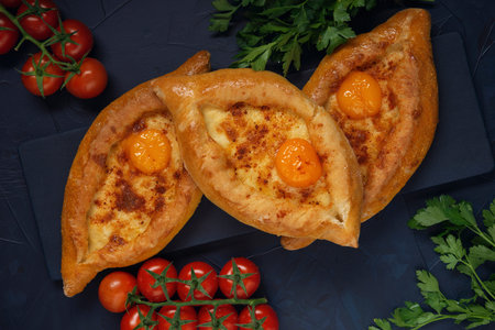 Adjarian Khachapuri â€“ Georgian cheese bread with tomatoes and parsley on black cutting board....
