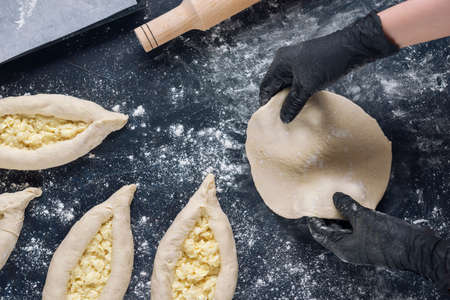 Woman in black shirt and black gloves holds rolled out yeast dough. Process of making bakery. The Adjarian Khachapuri Recipe â Georgian cheese bread.の写真素材