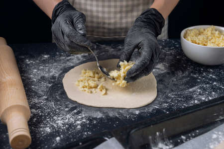 Woman in checkered apron and black gloves spread the filling on the dough. Process of making bakery. The Adjarian Khachapuri Recipe â Georgian cheese bread.の写真素材