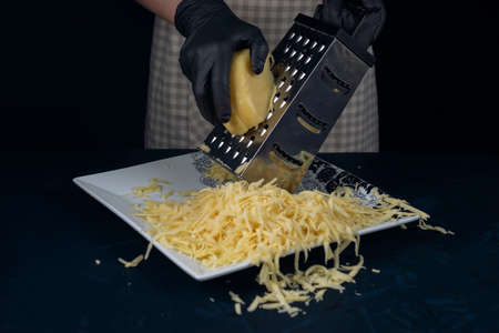 Woman in checkered apron rubs cheese on a grater. Home cooking. The Adjarian Khachapuri Recipe â Georgian cheese bread.の写真素材