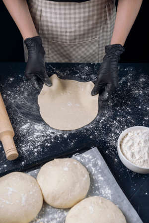 Woman in black shirt and black gloves holds rolled out yeast dough. Process of making bakery. The Adjarian Khachapuri Recipe â Georgian cheese bread.の写真素材
