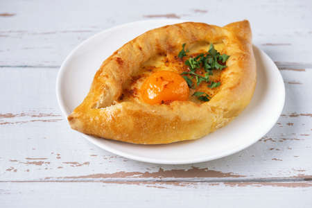 White plate with Adjarian Khachapuri â Georgian cheese bread on white Provence style background. Baked open pie with cheese and egg yolk filling.の写真素材