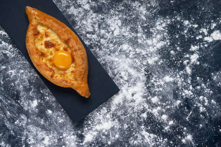 Adjarian Khachapuri â Georgian cheese bread. Baked open pie with cheese and egg yolk filling. Bakery with wheat flour on dark blue textured background. Flat lay. Space for text.の写真素材