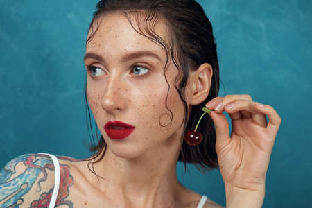 Close-up portrait of young freckled woman with the cherry berry.の写真素材