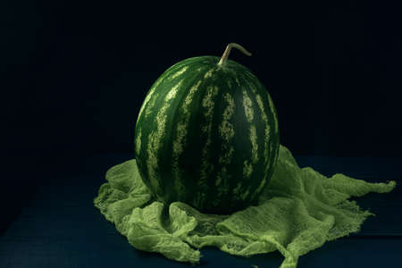 Whole green ripe watermelon on the green gauze napkin and dark blue wooden table.の写真素材