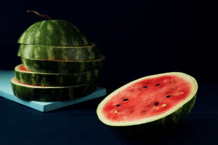 A slice and sliced watermelon on the dark blue wooden table.の写真素材