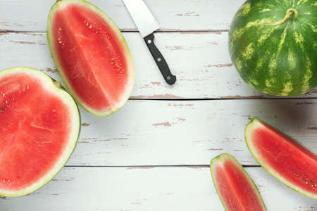One whole watermelon with pieces of sliced one and knife on the white wooden Provence style background. Flat lay.の写真素材