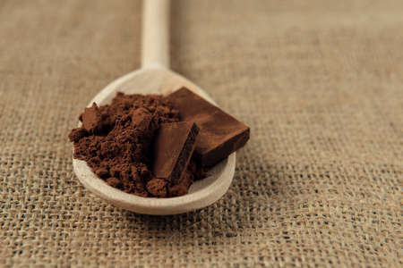 Cocoa powder with a few pieces of chocolate in wooden spoon on the burlap napkin. Space for text. Copy space.の写真素材