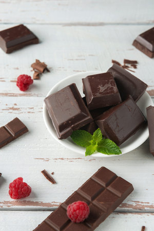 Pieces of chocolate with chocolate shavings, raspberry and mint on the white Provence style table.