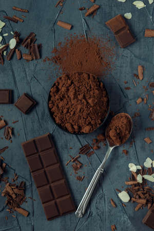 Bowl with cocoa, spoon, pieces of chocolate, chocolate shavings and almond flakes on the grey textured background. Top view. Flat lay.の写真素材