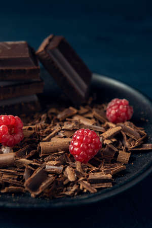 Chocolate pieces with chocolate shavings and raspberry in black plate on the dark wooden backgroundの写真素材