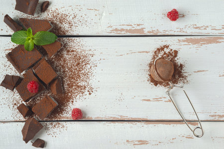 Pieces of chocolate, raspberry and mint covered with cocoa powder on the white Provence style table....