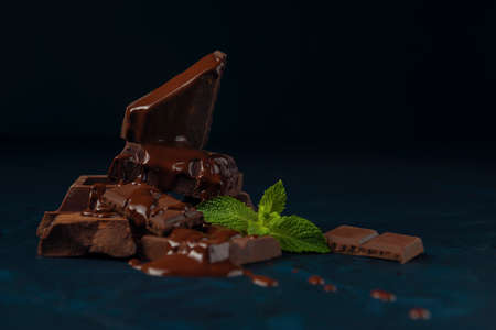 Chocolate pieces and mint leaves poured with liquid chocolate on the dark blue textured background.の写真素材