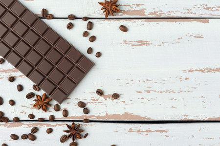 Chocolate bar with star anise and coffee grains on the white wooden Provence style table. Top view....