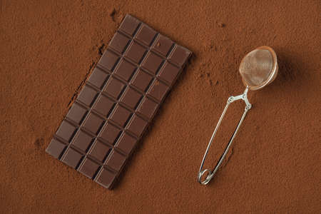 Chocolate bar and strainer on the cocoa powder background.の写真素材