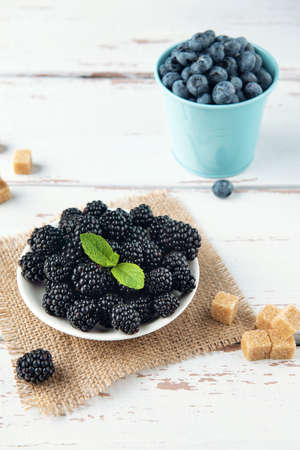 White plate with blackberry and blueberry bucket on the white Provence style wooden table.の写真素材