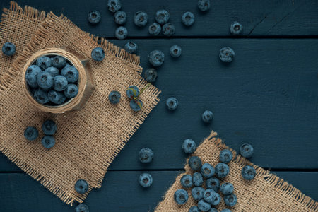 Bowl with ripe blueberry on burlap napkin and the dark wooden table. Flat lay. Copy space.