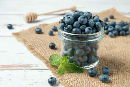 Glass jar of ripe blueberry with mint leaves on burlap napkin and the white Provence style wooden table.の写真素材