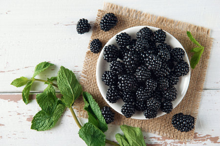 White plate with blackberry and with mint leaves on burlap and the white Provence style wooden...