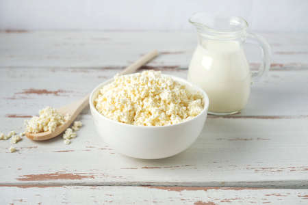 Bowl with cottage cheese and jug of milk on the white Provence style wooden tableの写真素材