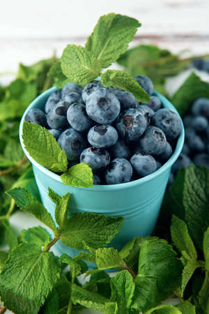 Small bucket with blueberry and mint leaves on the white Provence style wooden table. Close-up.の写真素材