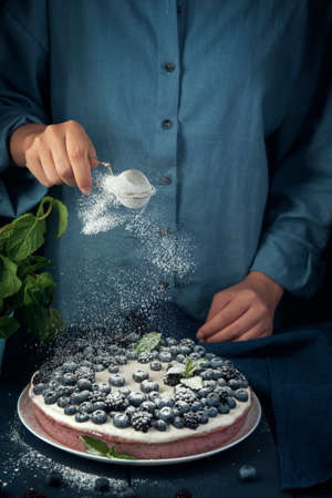 Female hands sprinkle with icing sugar cottage cheese casserole. Woman decorates cottage cheese pie with sugar powder.の写真素材