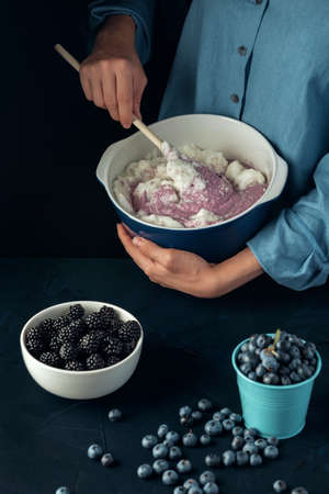 Female hand mixing berries and cottage cheese with wooden spoon. Cooking process. Cottage cheese casserole making.の写真素材