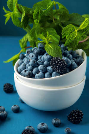 White bowl with mix blueberry, blackberry and mint leaves on the blue background.の写真素材