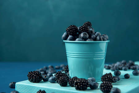 Blue bucket with mix blueberry and blackberry on the blue cutting board.の写真素材