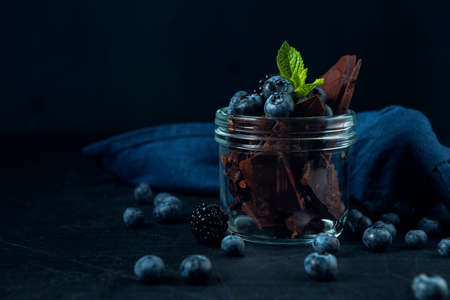 Glass jar with blueberry, blackberry, mint and chocolate pieces on the dark textured background.の写真素材