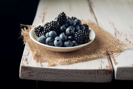 White plate with blackberry and blueberry on the burlap on the white wooden table.の写真素材