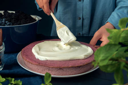 Female hand smears sour cream on the cottage cheese casserole. Woman decorating cottage cheese pie with cream. Top view.の写真素材
