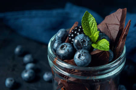 Close-up jar with blueberry, blackberry, mint and chocolate pieces on the dark textured background.の写真素材