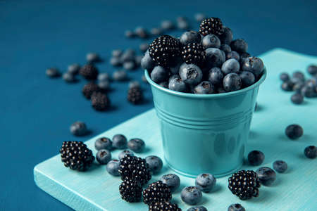 Blue bucket with mix blueberry and blackberry on the blue wooden backdrop.の写真素材