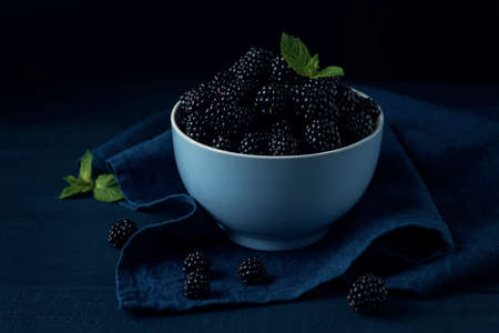 Bowl with ripe blackberry and mint leaves on blue napkin and the dark wooden table.の写真素材