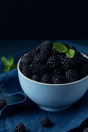 Bowl with ripe blackberry and mint leaves on the dark wooden table.の写真素材