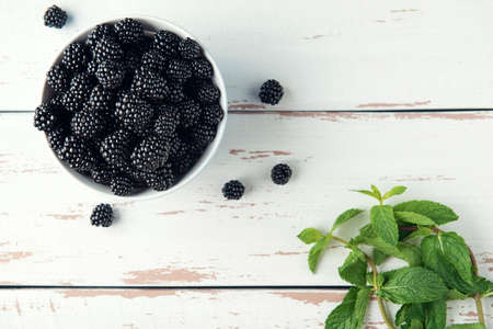 Bowl with ripe blackberry and mint leaves on the white Provence style wooden table. Flat lay. Copy space.の写真素材