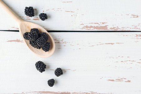 Wooden spoon with blackberry on the white Provence style table. Copy space. Flat lay.