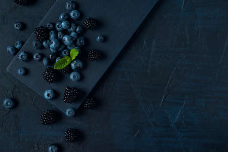 Scattered blueberry and blackberry on black cutting board and the dark textured background.の写真素材
