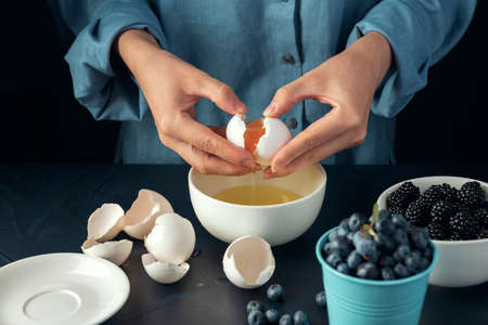 Close-up female hands break egg into the bowl. Bakery making. Cottage cheese casserole making.の写真素材