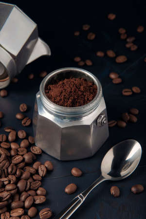 Coffee maker with ground coffee, coffee beans and metal spoon on the dark textured backgroundの写真素材