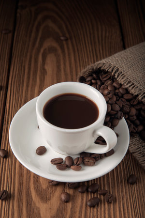 Cup of coffee with beans on the wooden textured tableの写真素材