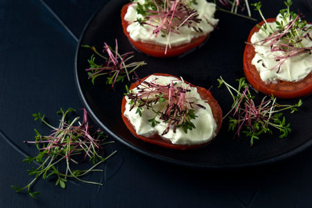 Black plate with tomato slices with cream and watercress microgreens on the dark textured backgroundの写真素材