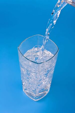 water being poured into a glass on blue background.の写真素材