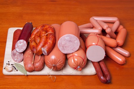 A variety of processed cold meat products, on a wooden cutting board.の写真素材